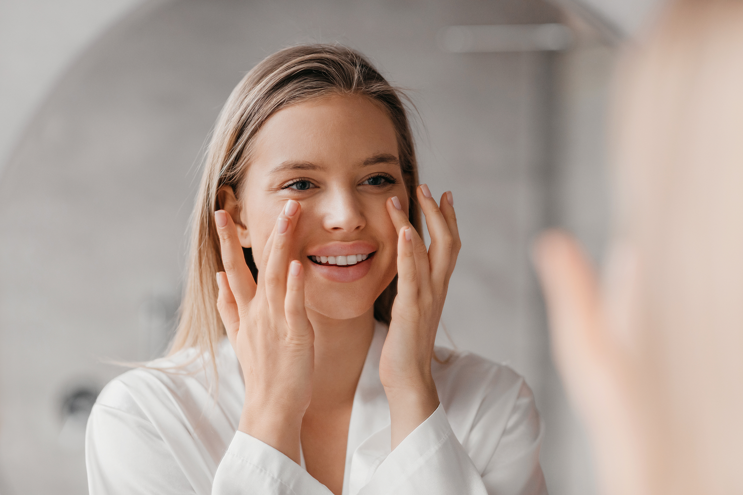 Smiling woman wearing white robe applying skincare